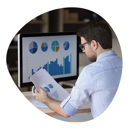 Studente che legge dei grafici sia in cartaceo, che su laptop in ufficio