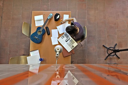 Student* al lavoro su una scrivania circondat* da fogli, libri e materiale di studio.
