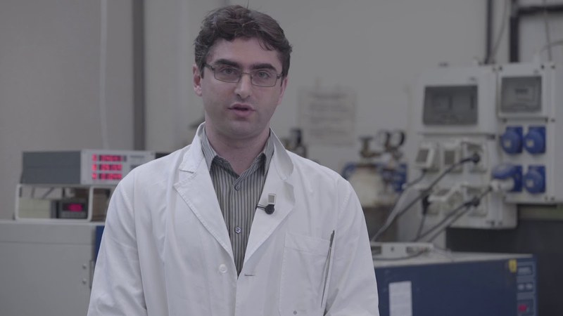 Un uomo con capelli castani, occhiali e camice bianco sta parlando all'interno di un laboratorio.