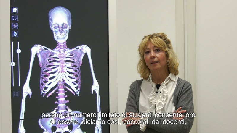 Una professoressa di fianco ad un proiettore con un'immagine di uno scheletro umano parla del corso.